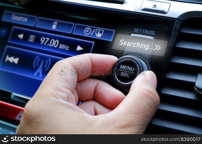 The driver adjusts his hand to seek for a radio station on the automobile radio dashboard 