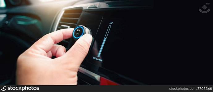 The driver hand is turning up or down the volume of the car music player or radio, panoramic banner with copy space on black background