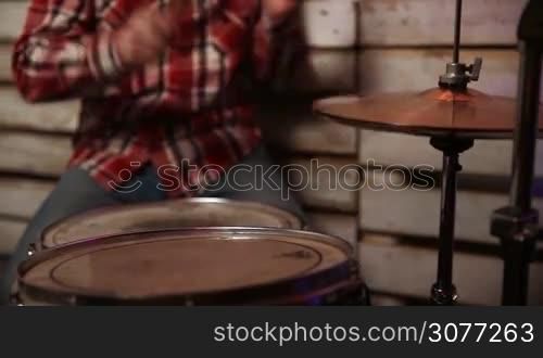 The drummer in action. Young male musician playing his drum kit and cymbals while performing with band in the club. Middle section of man with drumsticks playing his drum set and metal cymbals during rehearsal in garage.