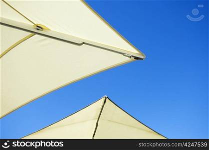 The edges of two white umbrellas in front of blue sky sunny background