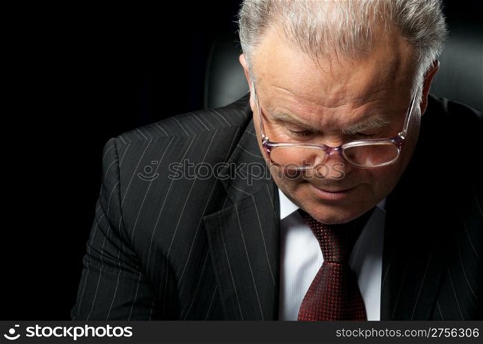 The elderly man in eyeglases reads the document. A photo against a dark background
