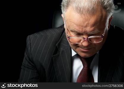 The elderly man in eyeglases reads the document. A photo against a dark background