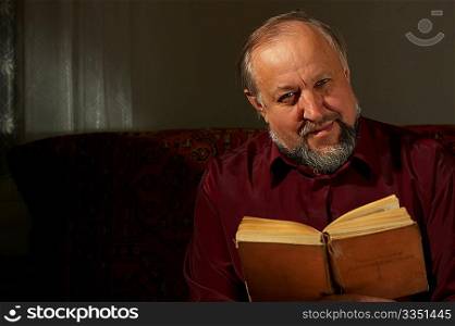 The Elderly man it is keen by reading of the book on a dark background