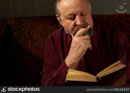 The Elderly man it is keen by reading of the book on a dark background. Wise man behind reading by the book