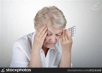 The elderly woman holds hands a head, going to accept tablets. Pain