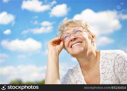 The elderly woman in glasses laughs against the sky. Pleasure by a life