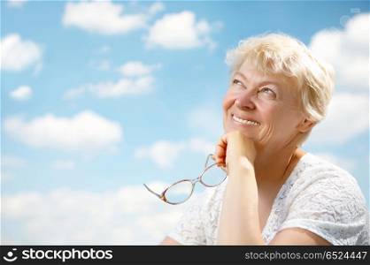 The elderly woman smiles and holds in hands glasses on a background of the blue sky. Grandmothers leisure