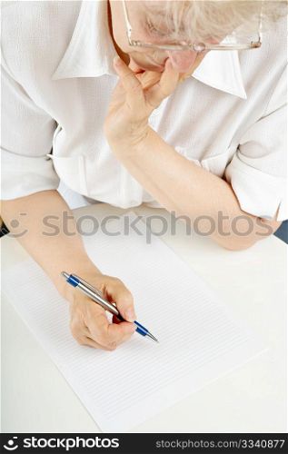 The elderly woman writes something on a sheet of paper
