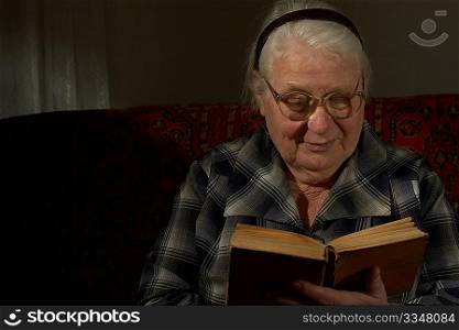 The Elderly women it is keen by reading of the book on a dark background