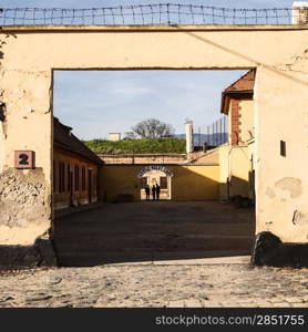 The entrance to the administrative area of the Little Fortress portion of the Theresienstadt concentration camp. At the end, the sign of Arbect Macht Frei (Labour Makes You Free) is visible over shadows of people.