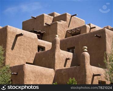 The facade of a hotel built to look like an old native American pueblo with adobe walls, square corners, exposed beams, and more.