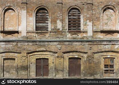 The facade of the old house is retro, a brown brick wall and arched windows boarded with wooden boards and rusty iron.. The facade of the old house is retro