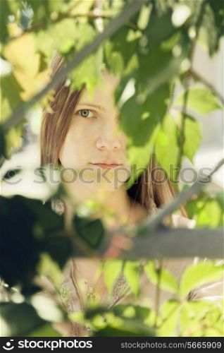 The face of a beautiful young woman in a green summer foliage on a sunny day