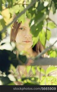 The face of a beautiful young woman in a green summer foliage on a sunny day