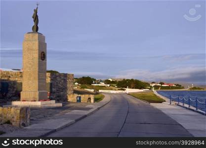 The Falklands War Memorial with Government House in the background - Port Stanley in the Falkland Islands (Islas Malvinas).