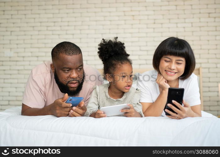 The family has fun and plays education games online with a smartphone at home in the bedroom. Concept of online education and caring from parents.