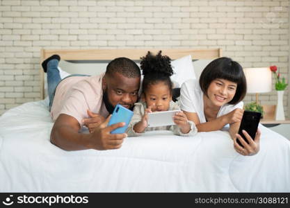 The family has fun and plays education games online with a smartphone at home in the bedroom. Concept of online education and caring from parents.