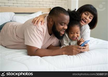 The family has fun and plays education games online with a smartphone at home in the bedroom. Concept of online education and caring from parents.
