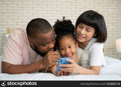 The family has fun and plays education games online with a smartphone at home in the bedroom. Concept of online education and caring from parents.