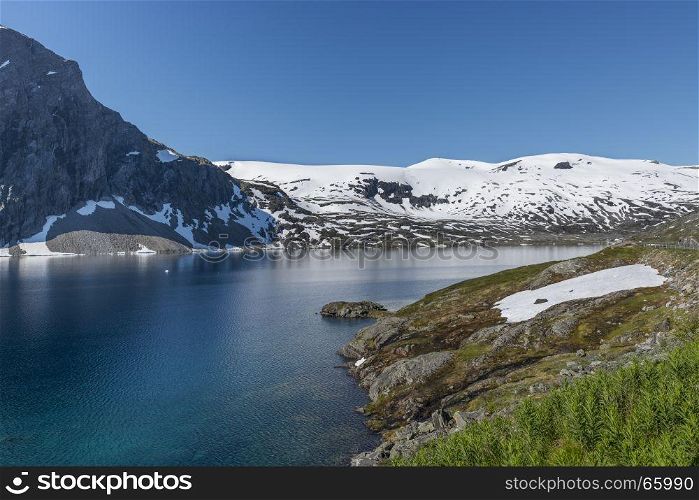 The famous road in Norway also called road 51 or the bygdin vegen near Bismo with blue water in the fjord and white snoiw on the mountains in summer