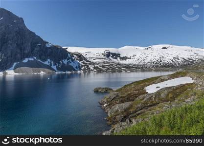 The famous road in Norway also called road 51 or the bygdin vegen near Bismo with blue water in the fjord and white snoiw on the mountains in summer