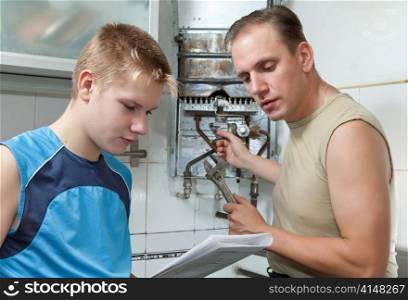 The father and the son-teenager together look the instruction on repair a gas water heater.