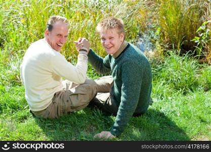 The father with the son are engaged in an armwrestling on the bank of a pond