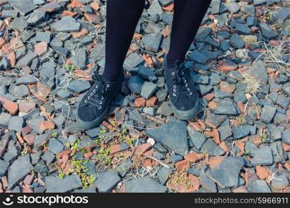 The feet and legs of a young woman standing on some gravel
