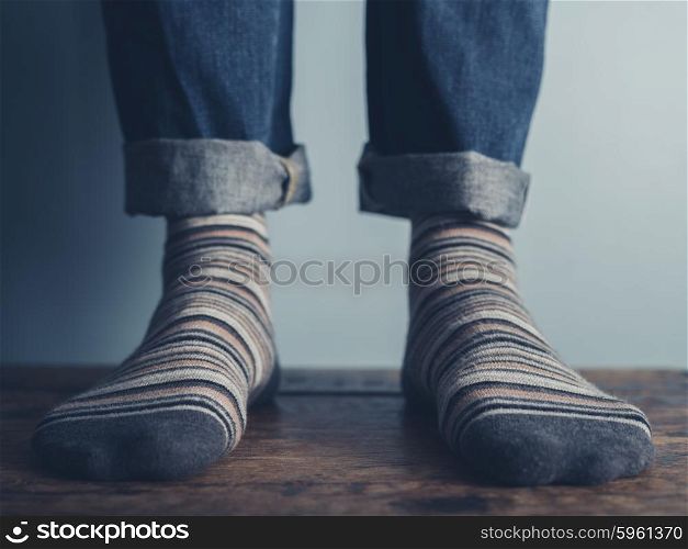 The feet of a man standing on a wooden floors wearing stripey socks