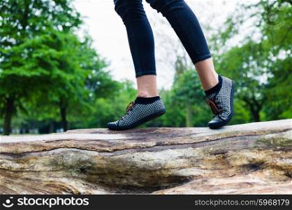 The feet of a trendy young woman as she is walking on a tree trunk in the park