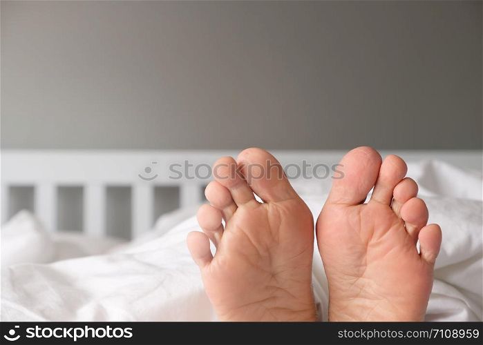The feet of a woman lying on a white bed in the morning.