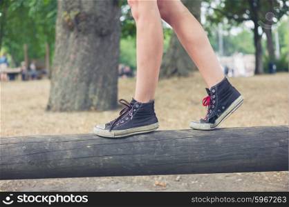 The feet of a young woman as she is walking on a wooden beam outside in the park