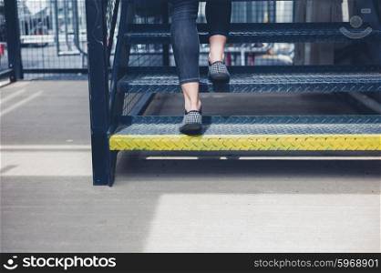 The feet of a young woman as she is walking up some metal stairs