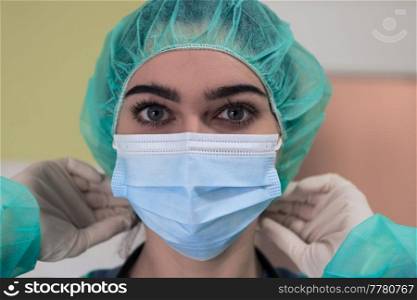 The female animal surgeon or veterinarian puts on a medical face mask. Doctor is preparing for surgery in the operation room. Medicine and healthcare. High quality photo. The female animal surgeon or veterinarian puts on a medical face mask. Doctor is preparing for surgery in the operation room. Medicine and healthcare