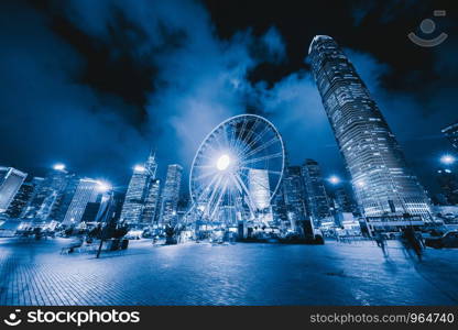 The ferris wheel, Hong Kong Observation Wheel at night, and amusement park for kids in holiday vacation and travel trip concept. Hong Kong City. Downtown and Victoria Harbour.