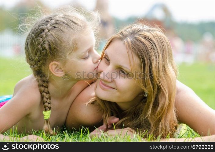 The five-year daughter kissing her mother lying on green grass lawn