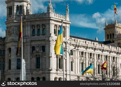 The flag of Spain and Ukraine flutter in the wind in front of Cibeles in Madrid, Spain. European Union and Spanish solidarity concept as Russia invaded Ukraine in February 2022. The flag of Spain and Ukraine flutter in the wind - solidarity against Russian invasion in 2022