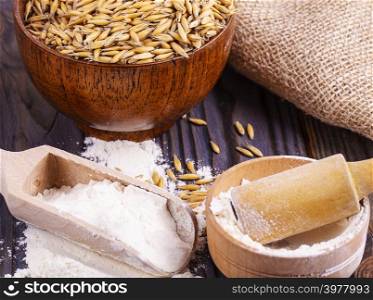 The flour pile and wheat grains in wooden spoon and bowl on wooden background
