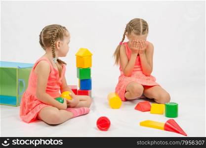 The four-year and six-year old girl playing in a European-style cubes, isolated on a light background