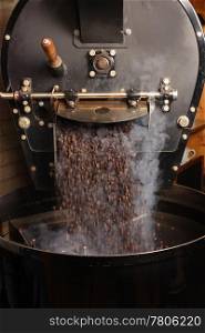 The freshly roasted coffee beans from a large coffee roaster being poured into the cooling cylinder. Motion blur on the beans.