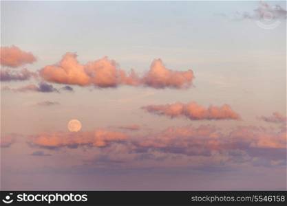 The full moon rises above a bank of cloud over the mediterrean in the pink light of sunset