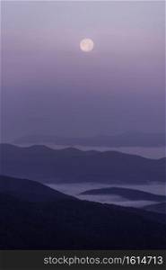 The full moon sets into a pallet of pinks, blues, and purples while valleys are filled with summer fog.
