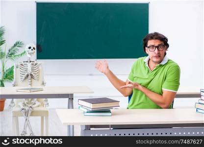 The funny male student in the classroom with skeleton . Funny male student in the classroom with skeleton