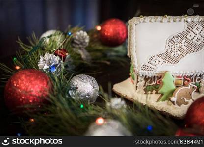the gingerbread house in the white glaze on the background of the Christmas wreath with Christmas decorations