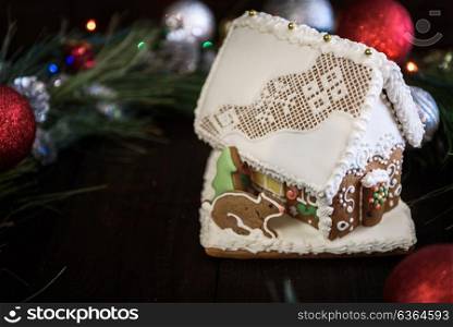 the gingerbread house in the white glaze on the background of the Christmas wreath with Christmas decorations