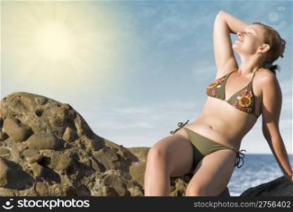 The girl acquiring a tan sitting on a stone