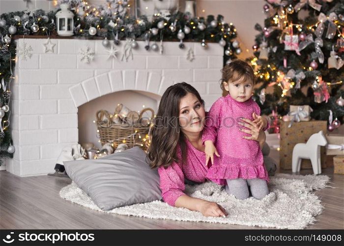 The girl and her mother lying on a blanket near the Christmas tree.. Portrait of a child and his mum in the Studio with Christmas decorations 9