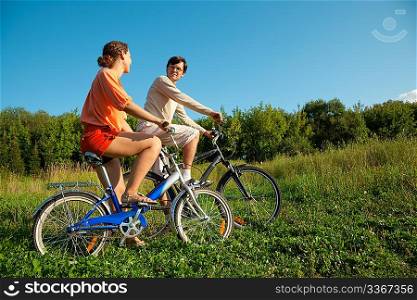 The girl and the man go for a drive on bicycles in a sunny day