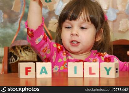 The girl and toy cubes. The child collecting a word family from cubes.