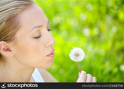 The girl blows on a dandelion on a background of a grass
